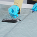 Hand model wearing protective blue gloves applying Gear Aid Seam Grip+ SIL Silicone Tent Sealant with a small brush on the seam of a grey tent 