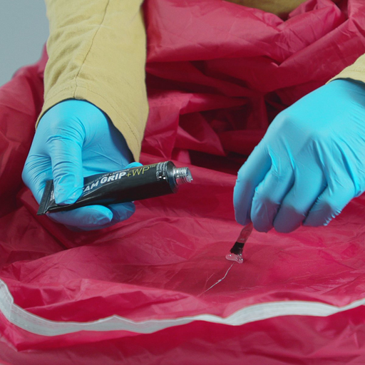 Gear Aid Seam Grip WP+ Adhesive and Sealant being applied with  the application brush to a tear in a red tent 