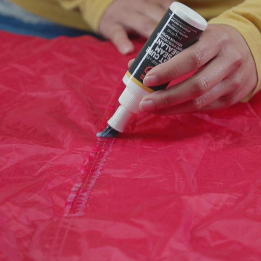 60ml Bottle of Gear Aid Seam Grip Fast  Cure Tent Seam Sealant being applied to the seam of a red tent 